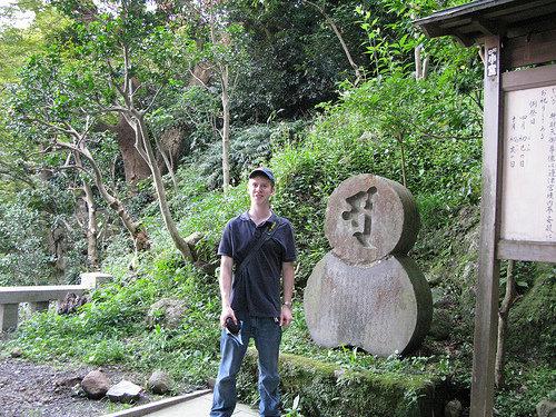 Henry beside a stone marker on a wooded path in Enoshima.